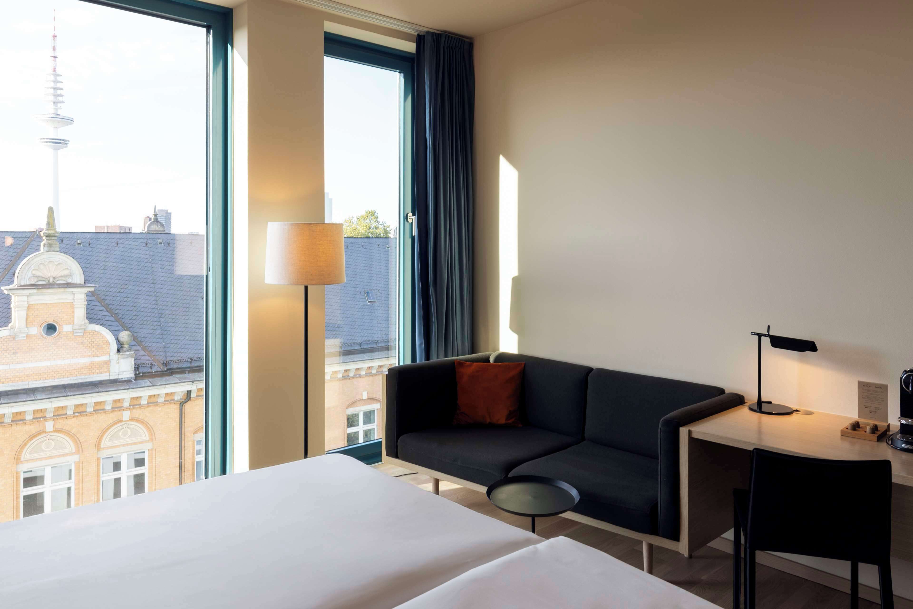 A hotel room with a bed, a desk, a chair, a sofa, and a lamp.