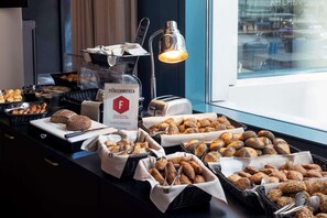 Un bufé con panes y pastelería variada, una cafetera y un cartel con el logotipo "FEINSCHMECKER".