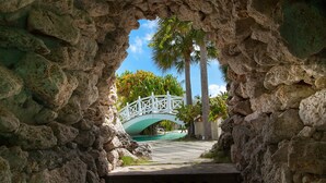 A stone archway leading to a bridge with a white railing, surrounded by palm trees and a clear sky. - The Marlin at Taino Beach Resort & Clubs (Freeport)