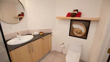 A bathroom with a round mirror, a sink, a toilet, and a shelf with towels.
