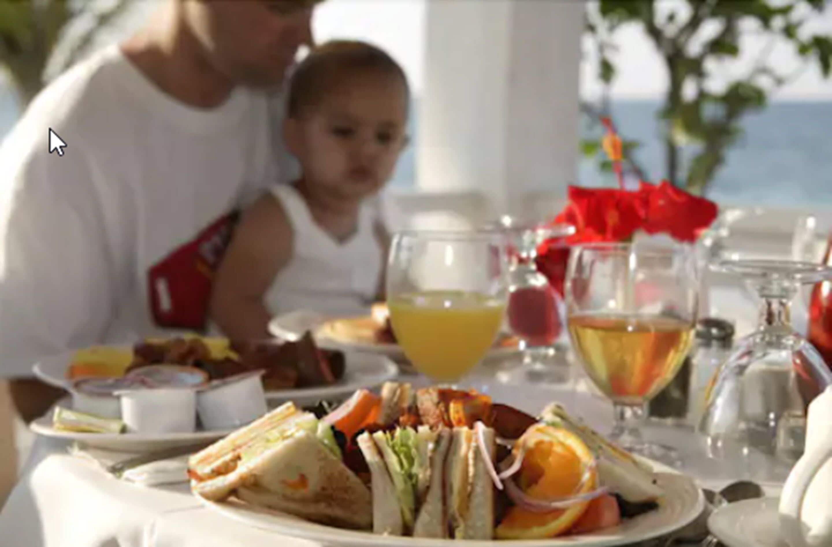 Una mesa de comedor con comida y bebidas, un niño, y vista al mar.