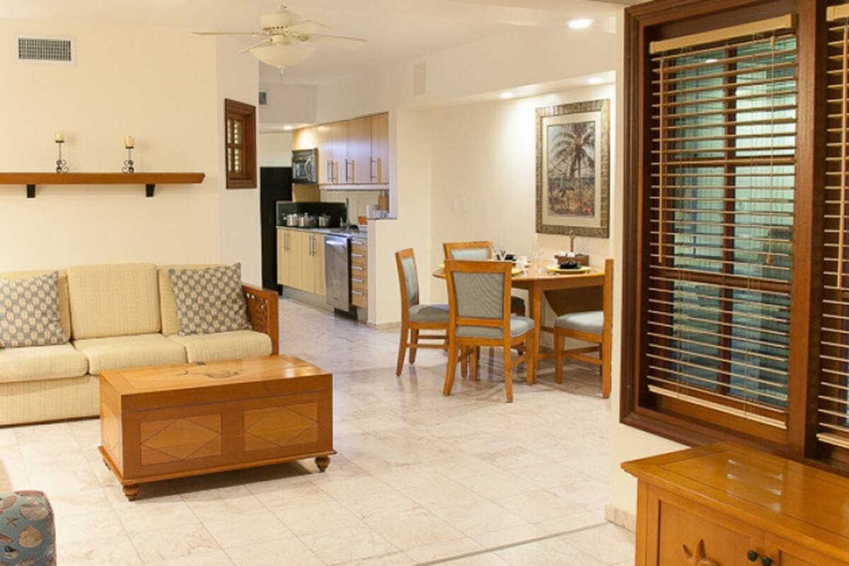 A living room with a sofa, coffee table, and dining area with chairs. There is a kitchen in the background.