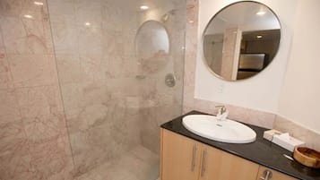 A modern bathroom with a marble shower wall, a round mirror, and a wooden vanity with a sink.