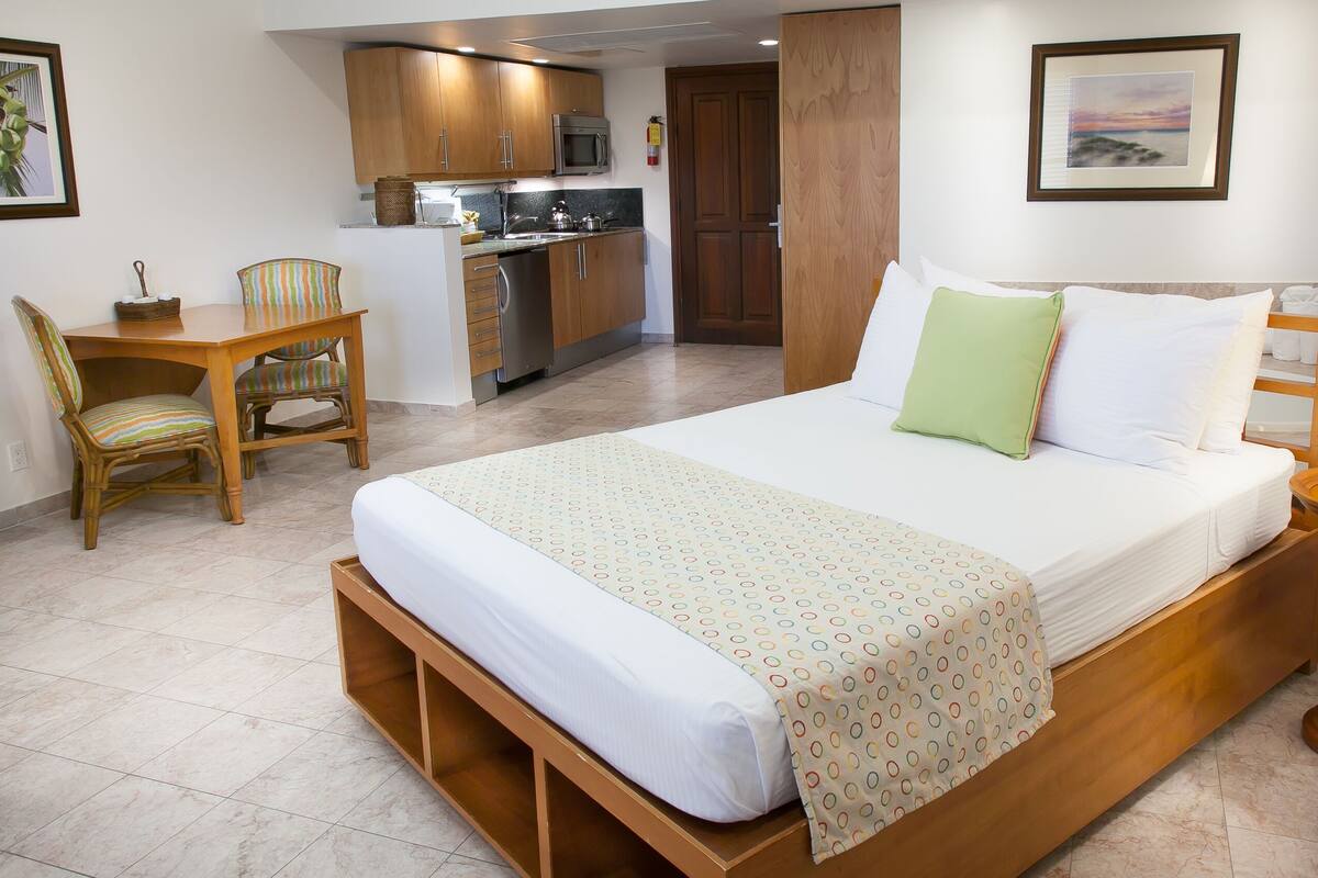 A hotel room with a bed, a desk, a chair, a kitchenette, and a bathroom.