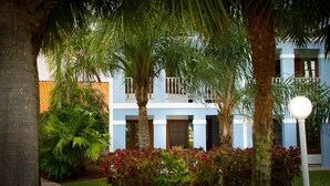 A two-story building with a blue exterior, surrounded by palm trees and a well-maintained garden with red-leafed plants. - The Marlin at Taino Beach Resort & Clubs (Freeport)