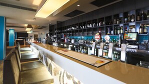 Una zona de bar moderna con una barra larga, asientos y una estantería bien surtida de licores.
