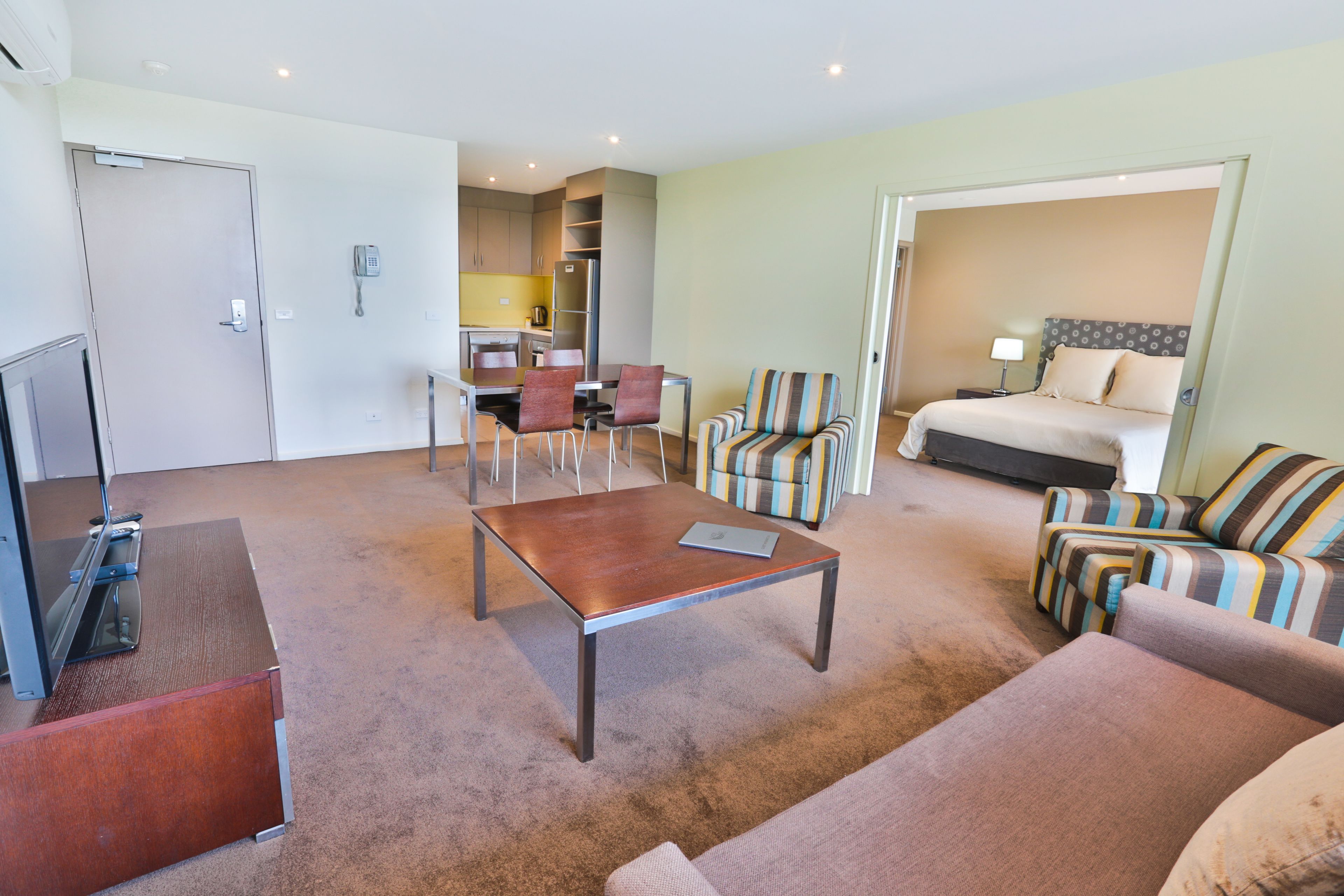 A hotel room with a bed, a TV, a coffee table, and two armchairs.