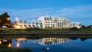Un hotel de varios pisos con su reflejo en el agua, que presenta un diseño arquitectónico moderno con balcones y techo plano.