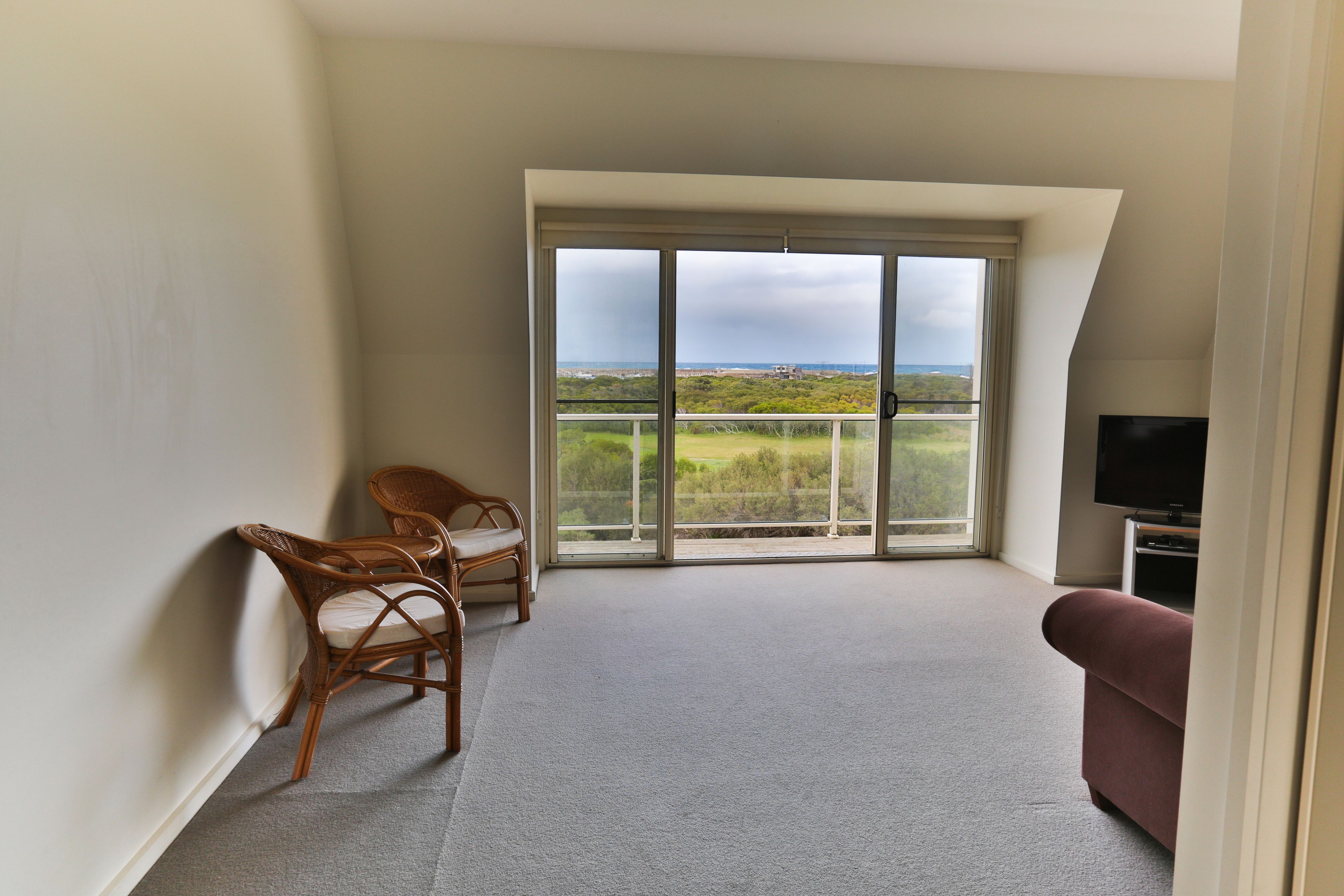 Un balcon avec vue sur la campagne, une télévision et deux fauteuils en osier.