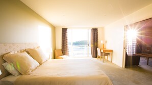 Habitación de hotel con una cama grande, un escritorio y vista al mar a través de la ventana.