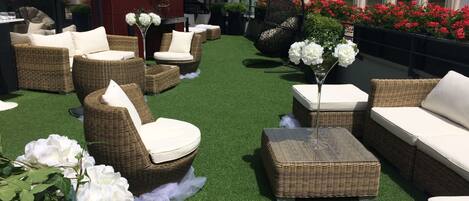 Un patio en la azotea con mobiliario de mimbre, césped artificial y plantas en macetas.