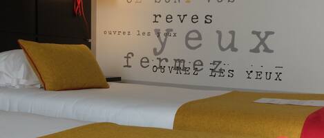 A hotel room with a bed, a wall with French text, and a lamp.
