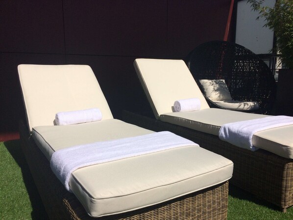 Dos sillones de relax con cojines blancos y estructura de mimbre, ubicados sobre césped artificial.