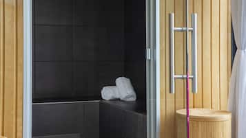 A modern bathroom with dark tiles, a wooden bench, and a small wooden stool.