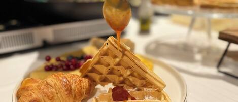 A plate with waffles, a croissant, and berries, with syrup being poured on the waffles.