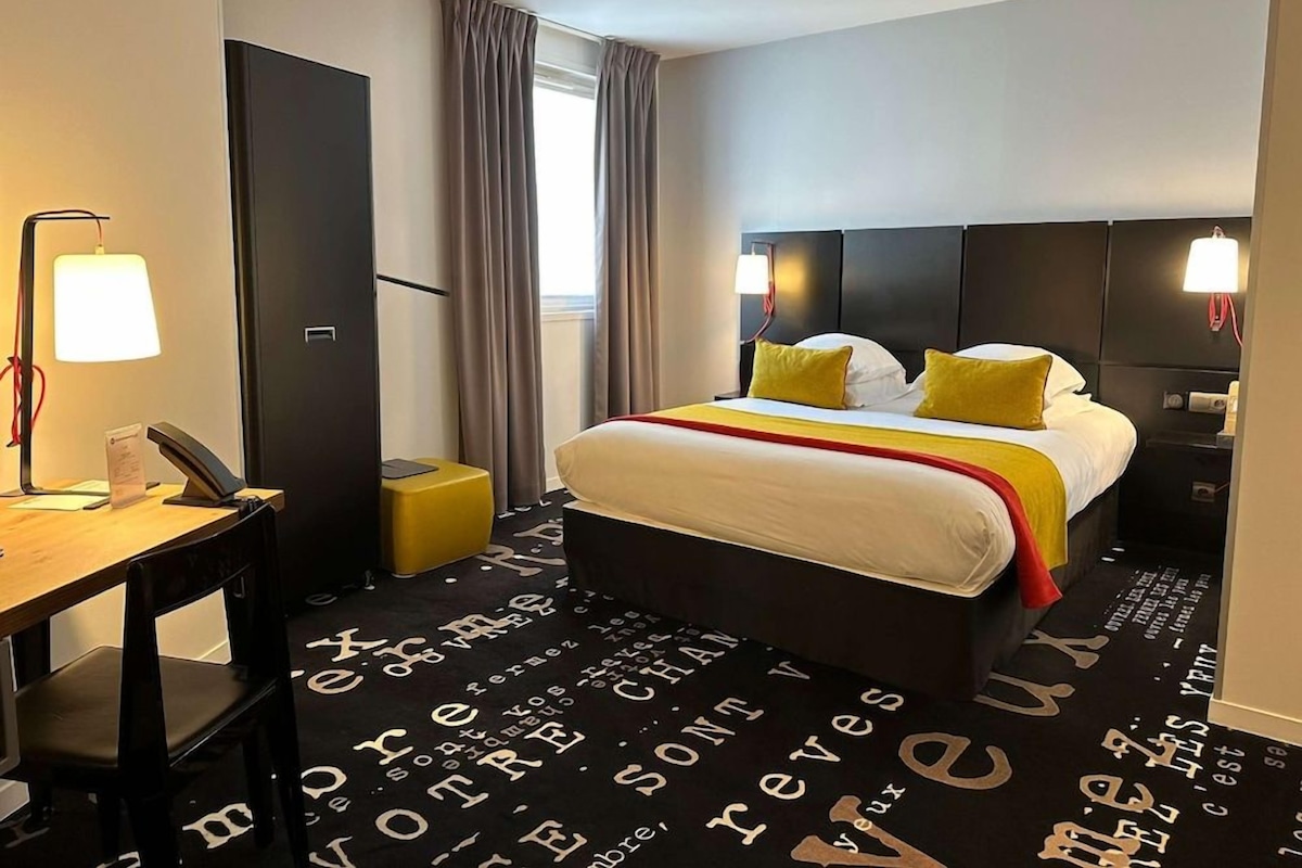 Ein Hotelzimmer mit Bett, Schreibtisch, Stuhl, Lampe, Kleiderschrank und einem Fenster mit Vorhängen.