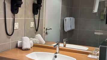 A modern bathroom with a wooden vanity, a white sink, a mirror, and two hair dryers mounted on the wall.