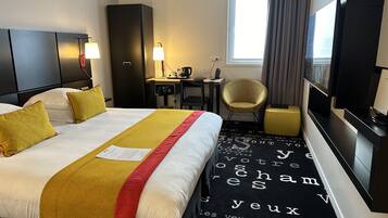 A hotel room with a bed, a desk, a chair, a television, and a window with curtains.