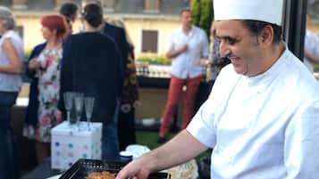 Un chef prepara comida al aire libre con una parrilla, rodeado de gente.