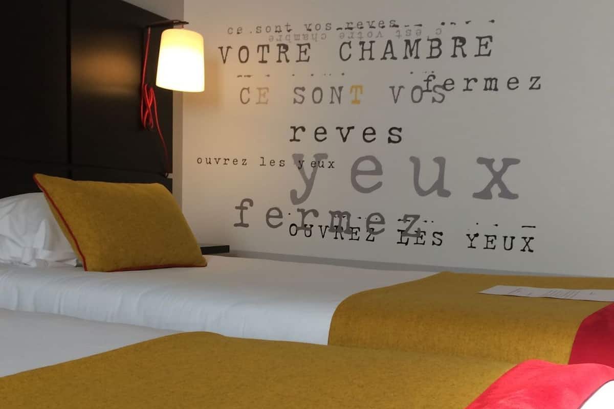 Una habitación de hotel con una cama, una pared con texto en francés y una lámpara.