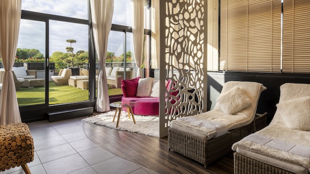 A modern lounge area with a large window, wicker lounge chairs, a pink sofa, and a decorative screen. - Best Western Plus Thionville Centre (Thionville)