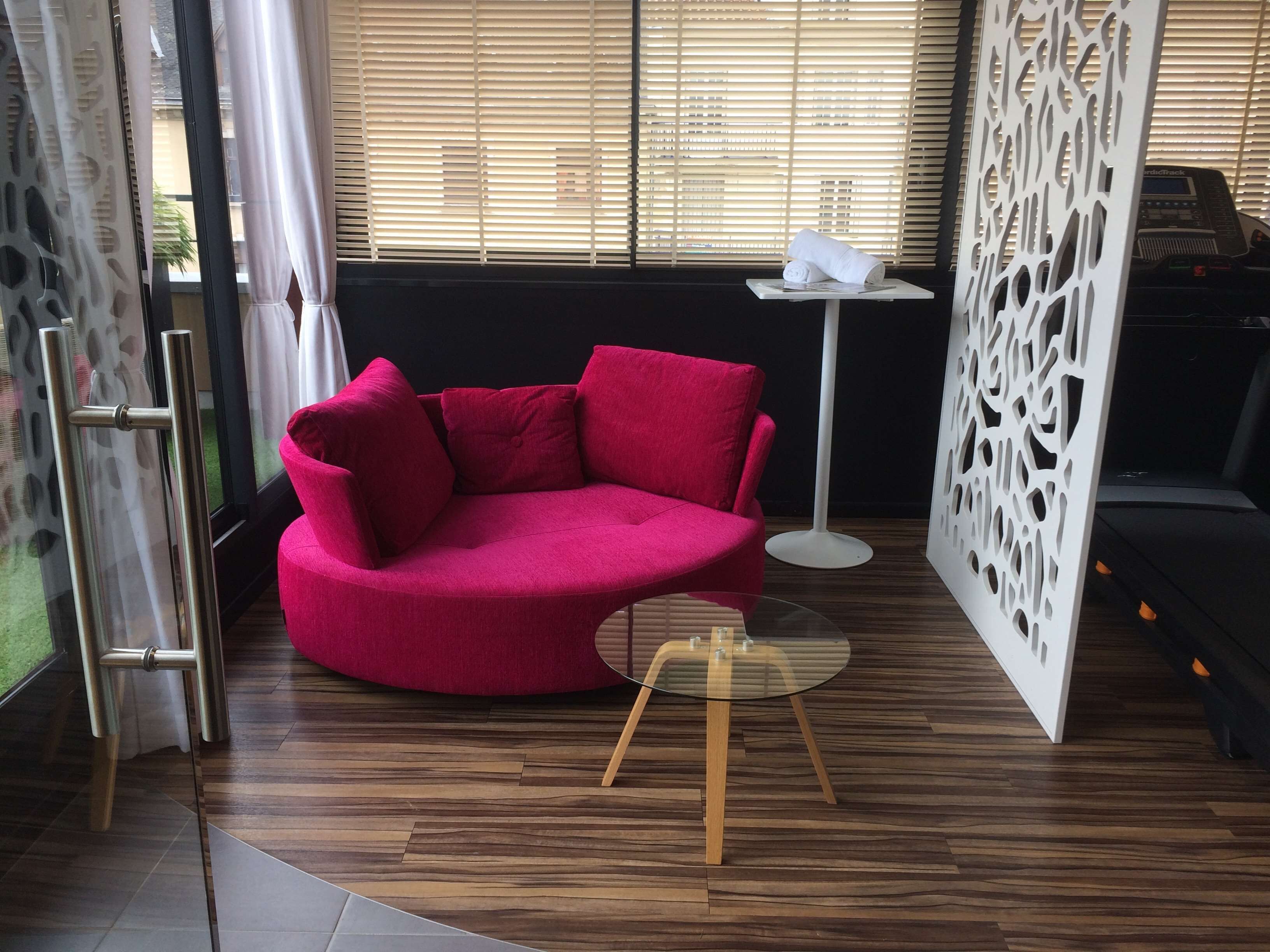 A modern living room with a curved red sofa, a small round glass table with wooden legs, and a decorative white panel.