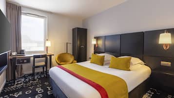 A hotel room with a large bed, a desk with a chair, a TV, and a window with curtains.