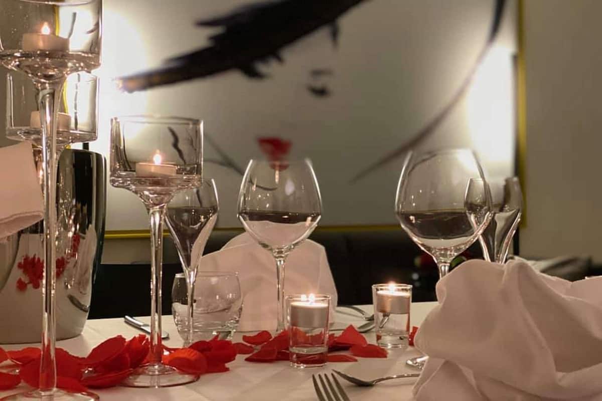 Una mesa dispuesta para una comida, con copas de vino, velas y pétalos de rosa.