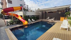 A swimming pool with a slide, surrounded by lounge chairs and a wooden deck. - Baan Manthana Hotel (Hua Hin)