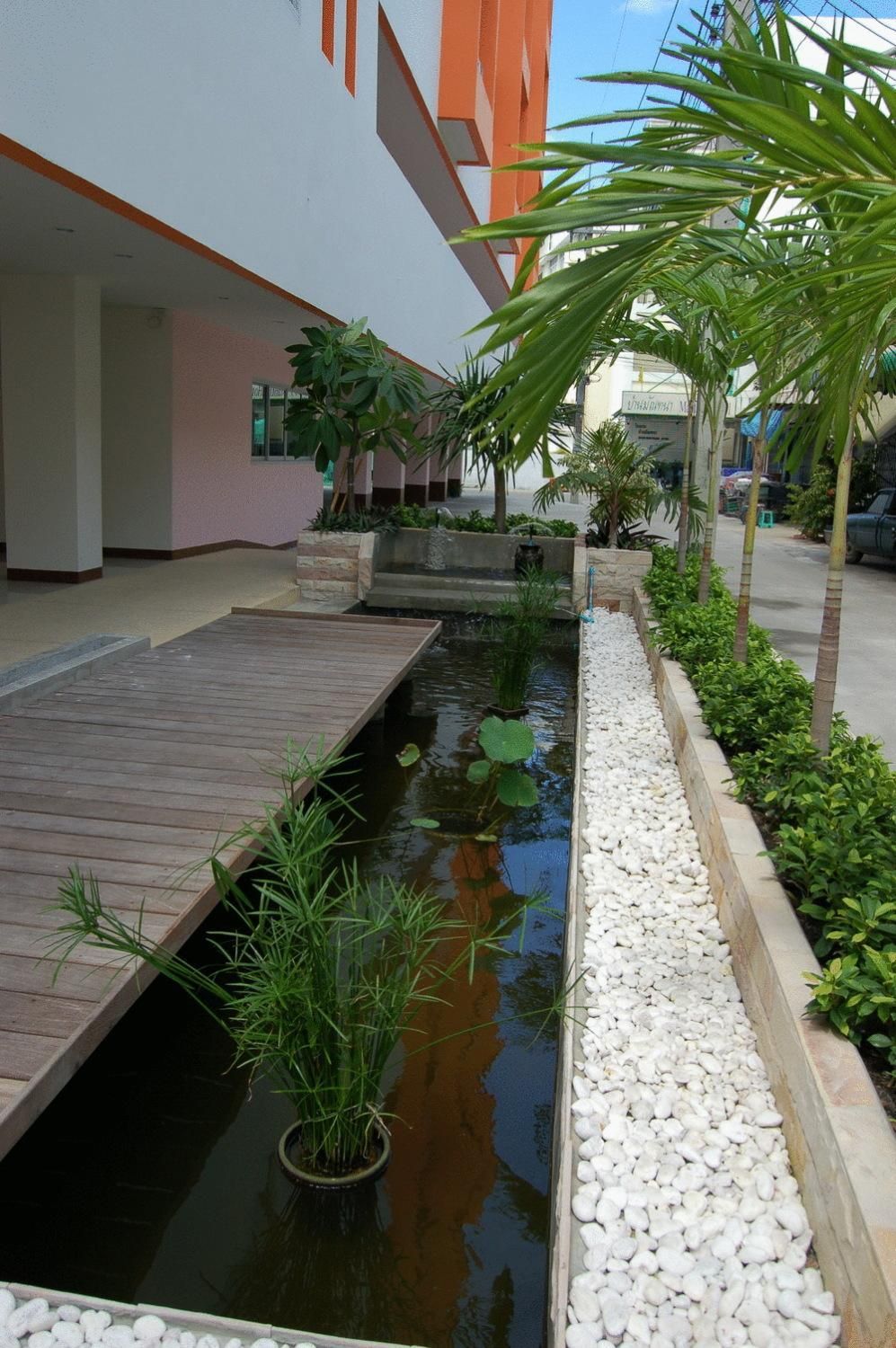 A tranquil indoor water feature with a wooden deck, surrounded by plants and a pebble-lined walkway.