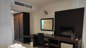 A hotel room with a bed, a desk with a chair, a television, a mini-fridge, and a mirror. - Baan Manthana Hotel (Hua Hin)