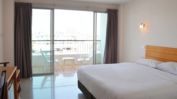 A hotel room with a bed, a desk, a chair, a balcony with a view of the city, and a sliding glass door. - Baan Manthana Hotel (Hua Hin)