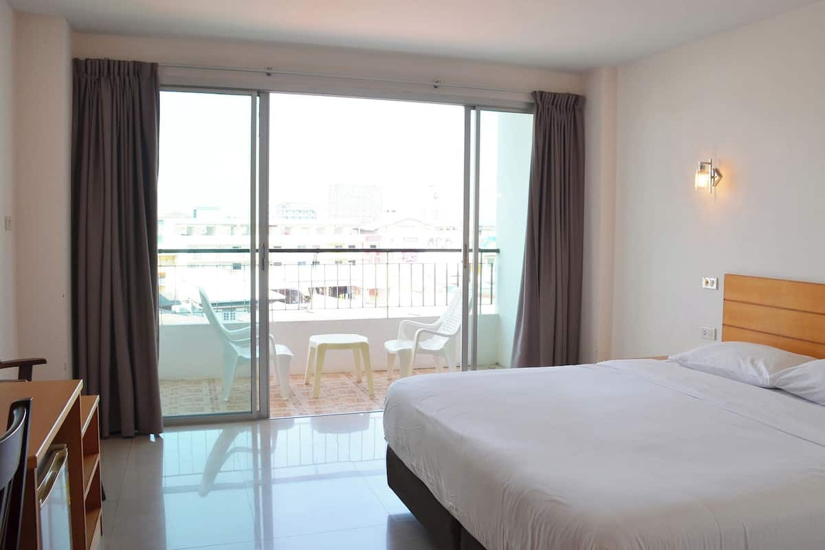 Een hotelkamer met een bed, een bureau, een stoel, een balkon met uitzicht op de stad en een schuifdeur.