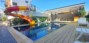 A swimming pool with a slide, lounge chairs, and a modern building in the background.