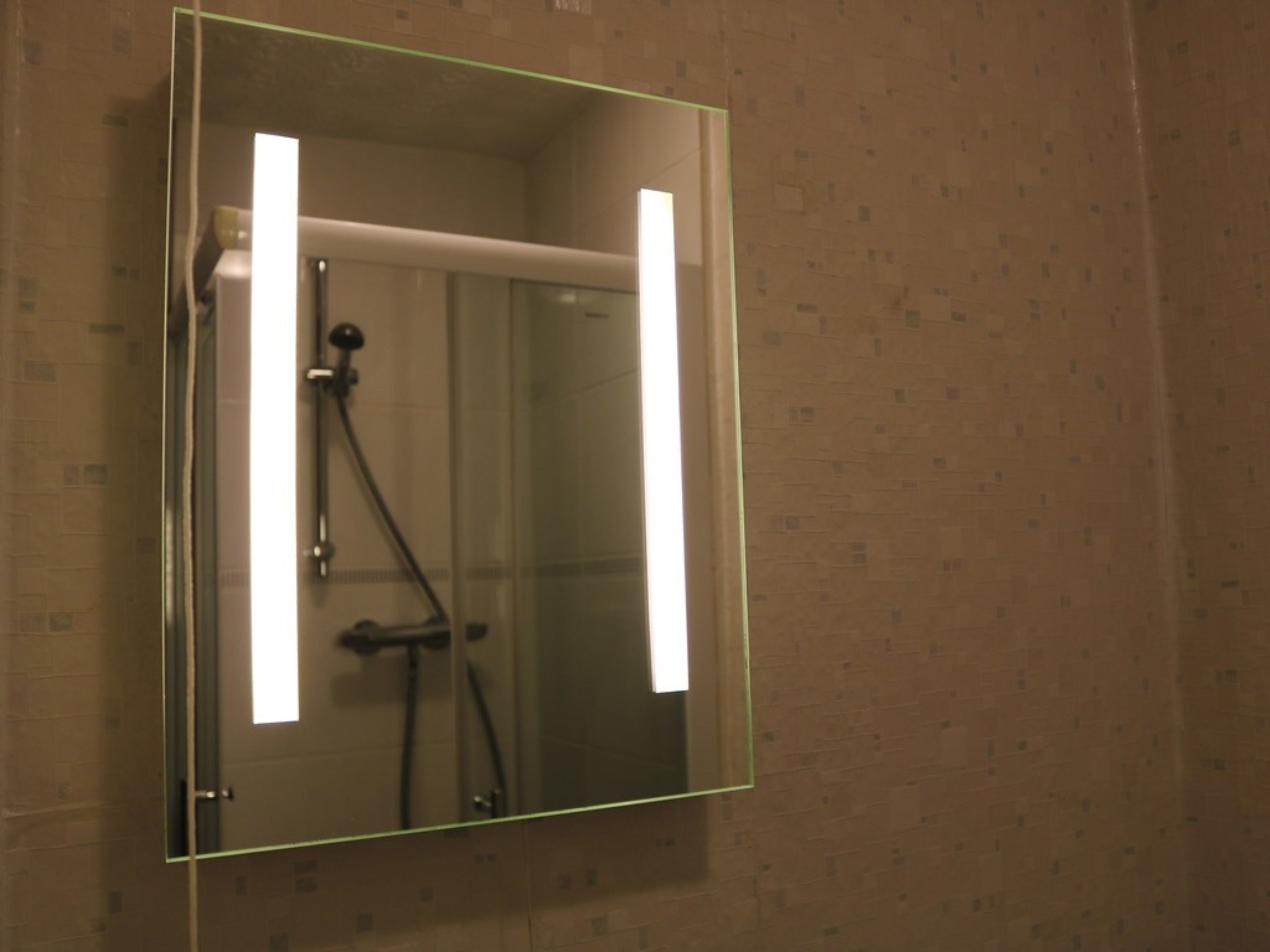 A bathroom with a glass-enclosed shower, a visible towel rack, and a mirror with a light strip.