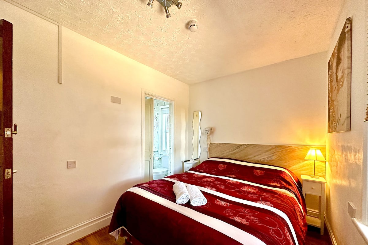 Ein Hotelzimmer mit einem großen Bett, einem Nachttisch, einer Lampe und einer Tür zu einem Badezimmer.