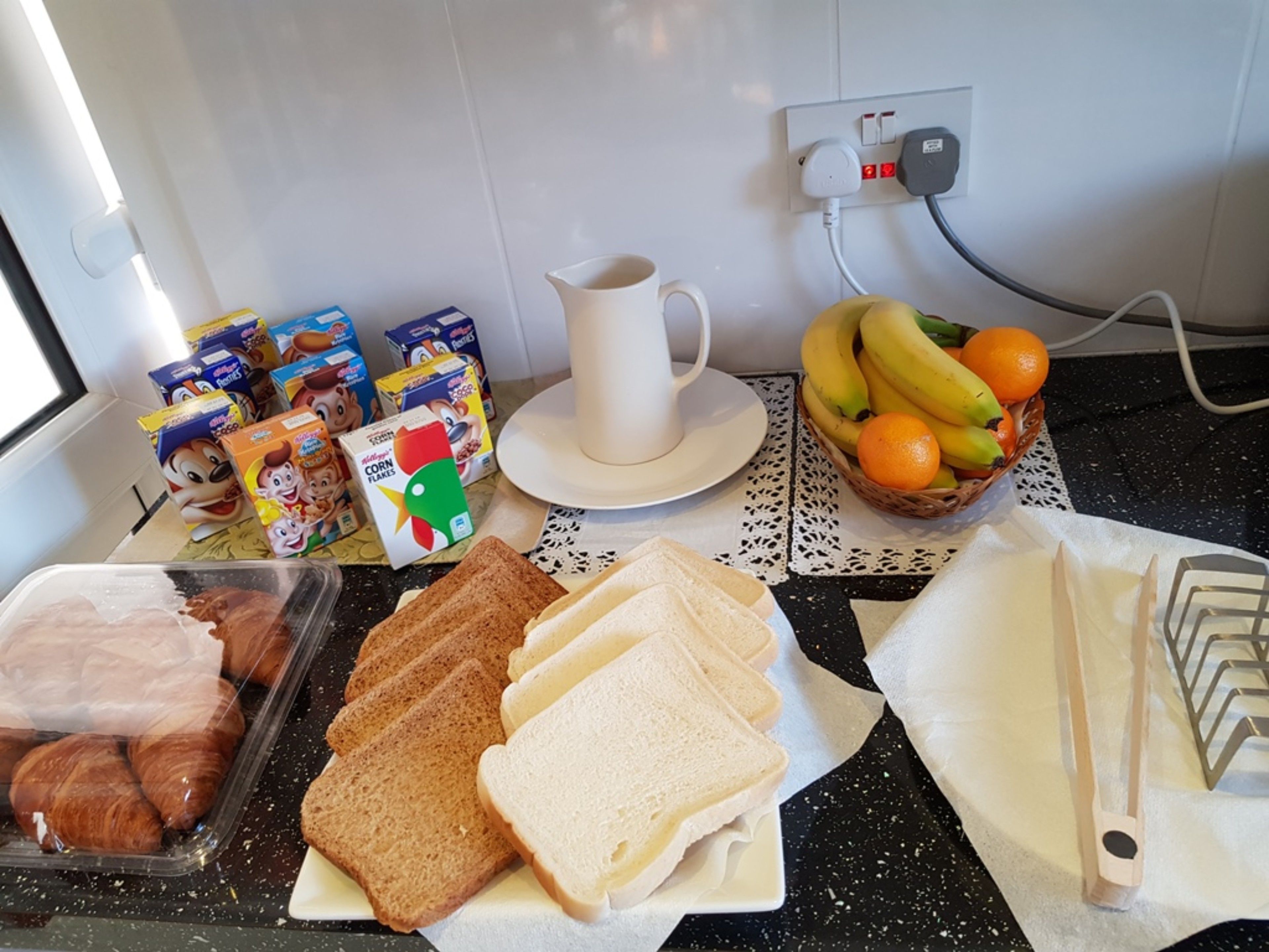 A kitchen counter with breakfast items including bread, eggs, cereal, and fruit.