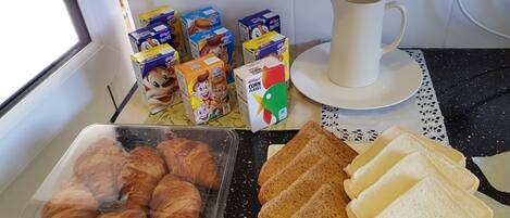 A breakfast setup with croissants, bread, cereal boxes, and a coffee cup on a kitchen counter.
