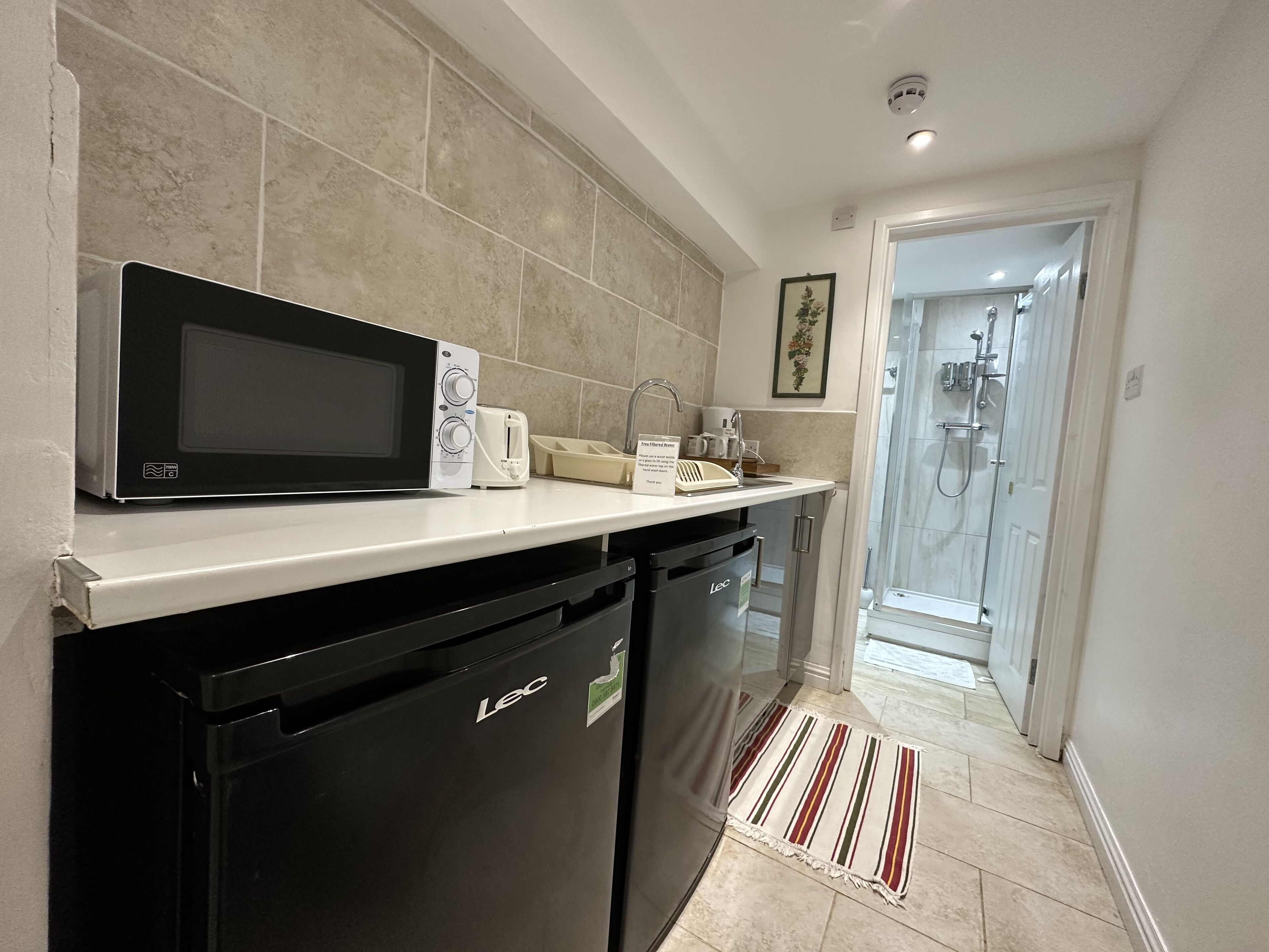 A compact kitchen with a microwave, toaster, and dishwasher. A shower is visible through an adjacent door.