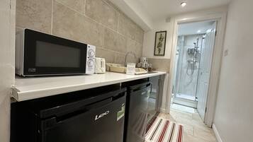 A compact kitchen with a microwave, toaster, and dishwasher. A shower is visible through an adjacent door.