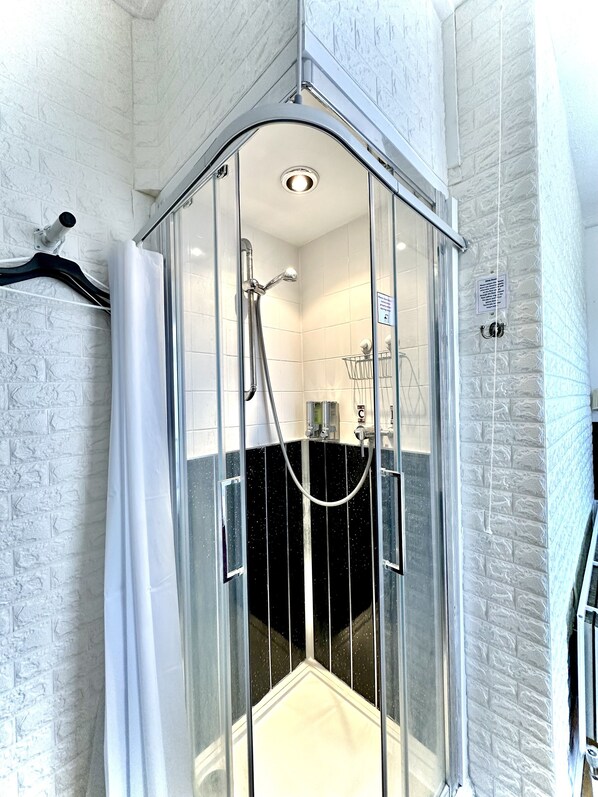 Una cabina de ducha con paredes de vidrio, cortina blanca, toallero y una toalla visible.