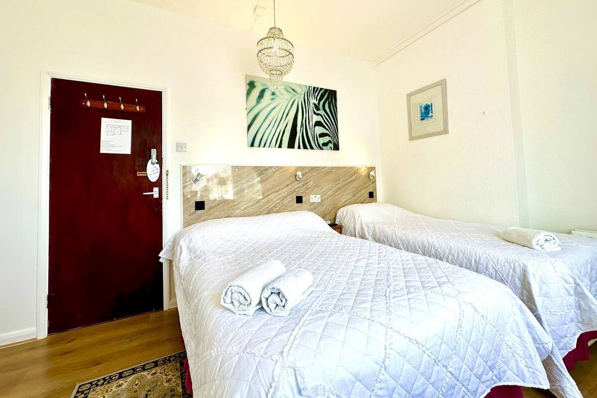 Ein Hotelzimmer mit zwei Betten, einem hölzernen Kopfteil, einer Kristallleuchtre, einem Zepra-Muster-Kunstwerk und einer roten Tür.