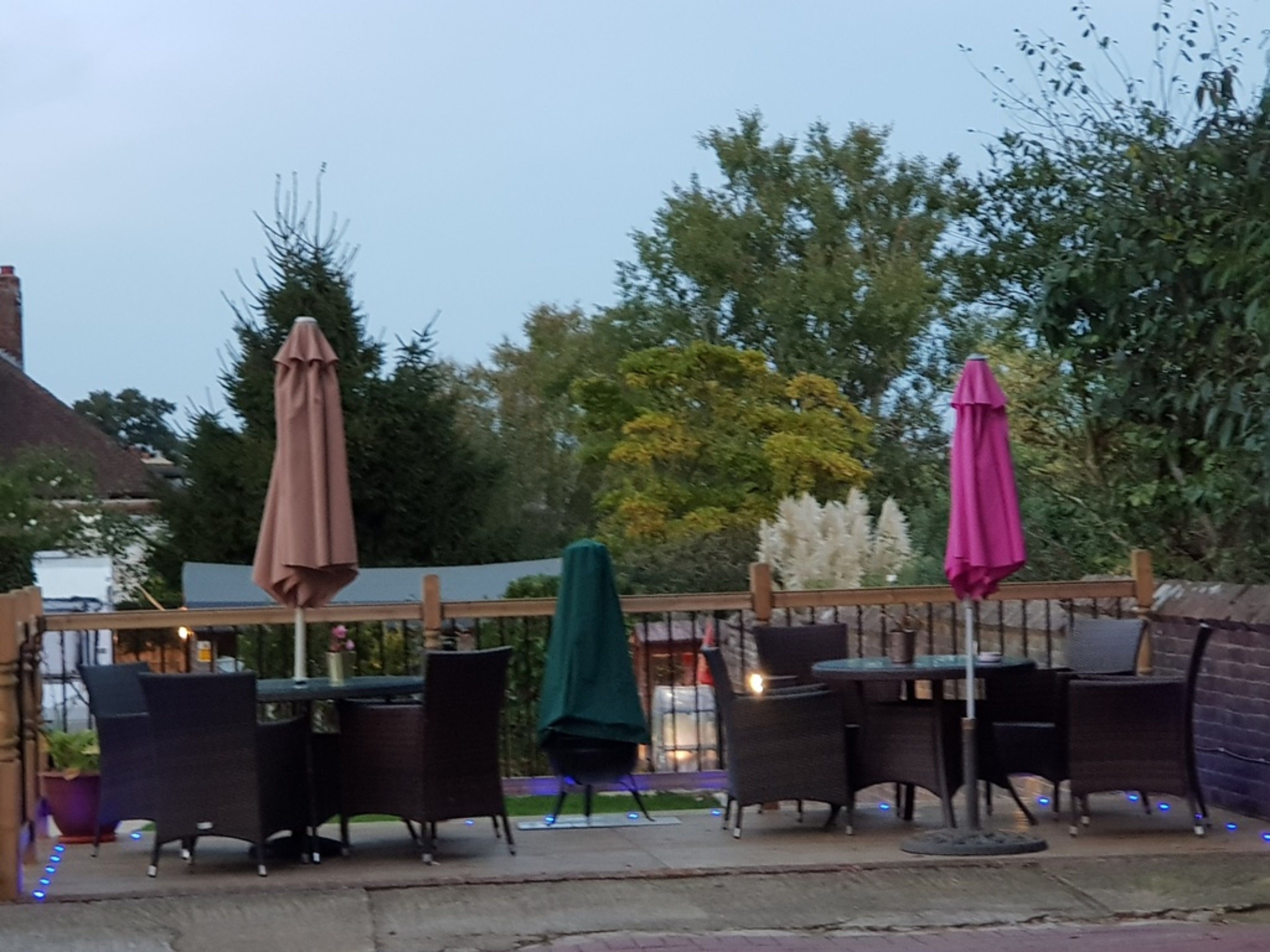 An outdoor patio with tables and chairs, surrounded by a wooden fence and trees.