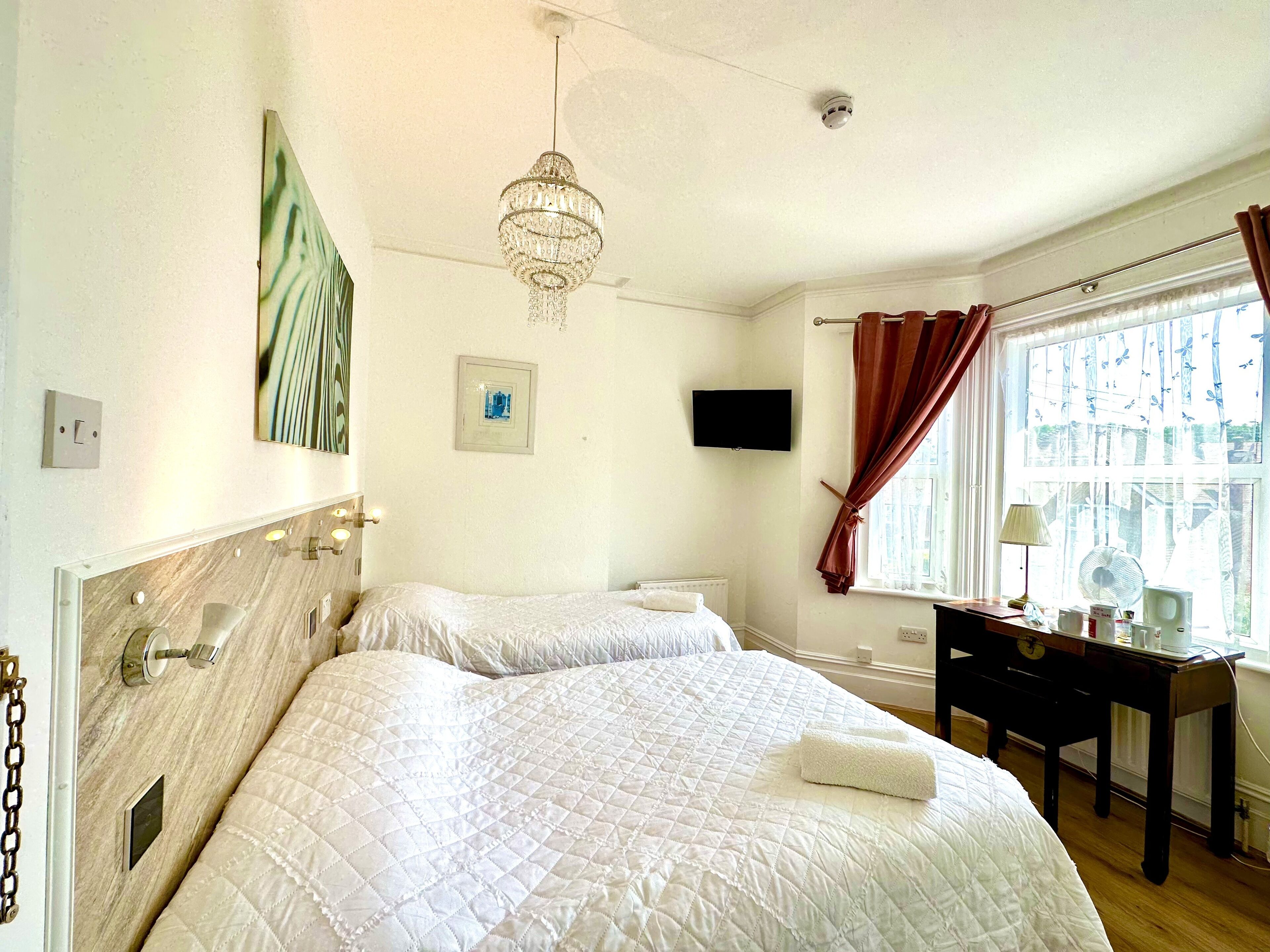 A hotel room with two beds, a desk, a TV, and a window with curtains.