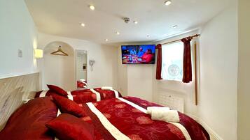 A hotel room with a large bed, a TV, a mirror, and a window with curtains.