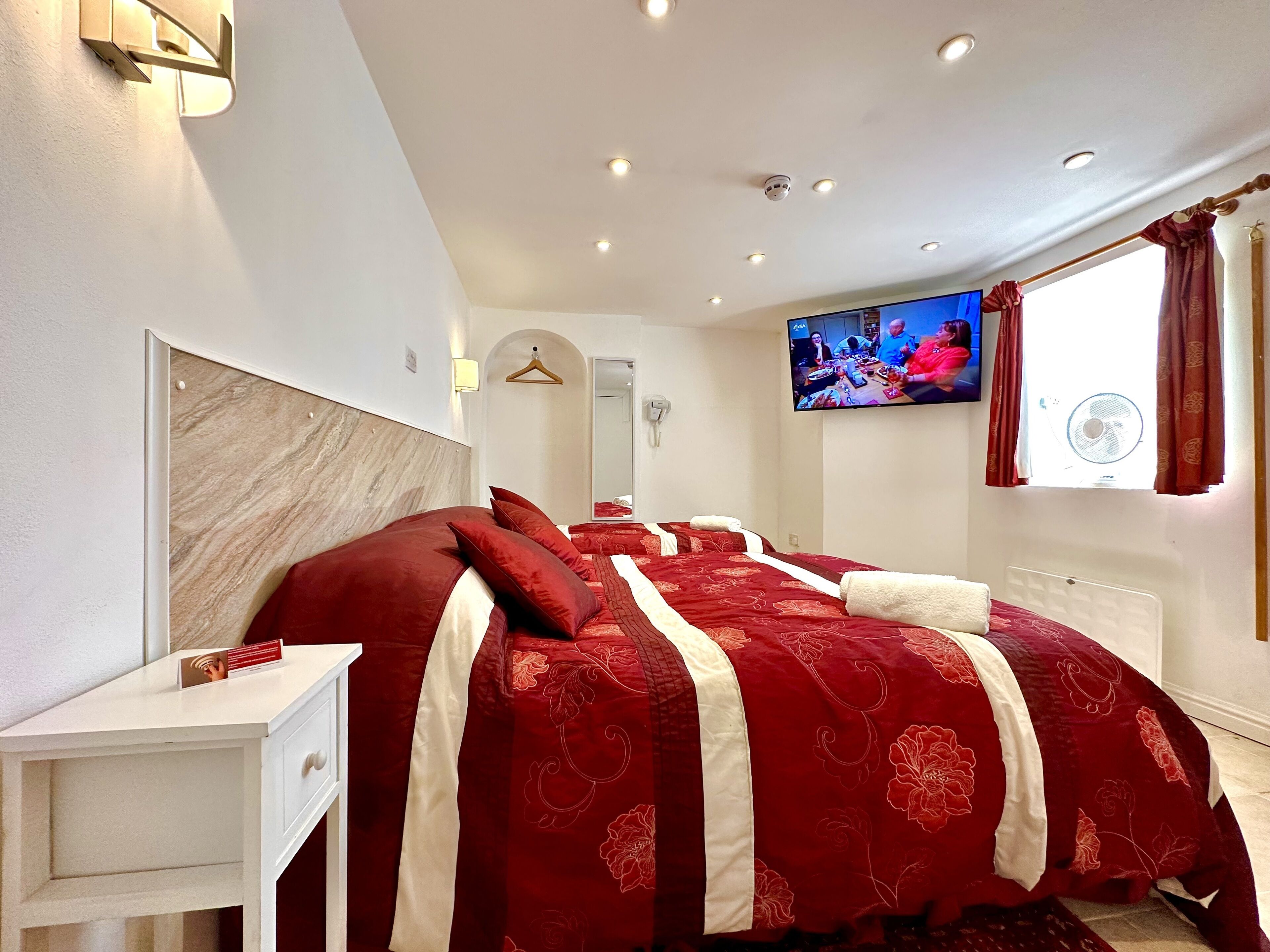 Une chambre d’hôtel avec un grand lit, une table de chevet, un téléviseur fixé au mur et une fenêtre avec des rideaux.