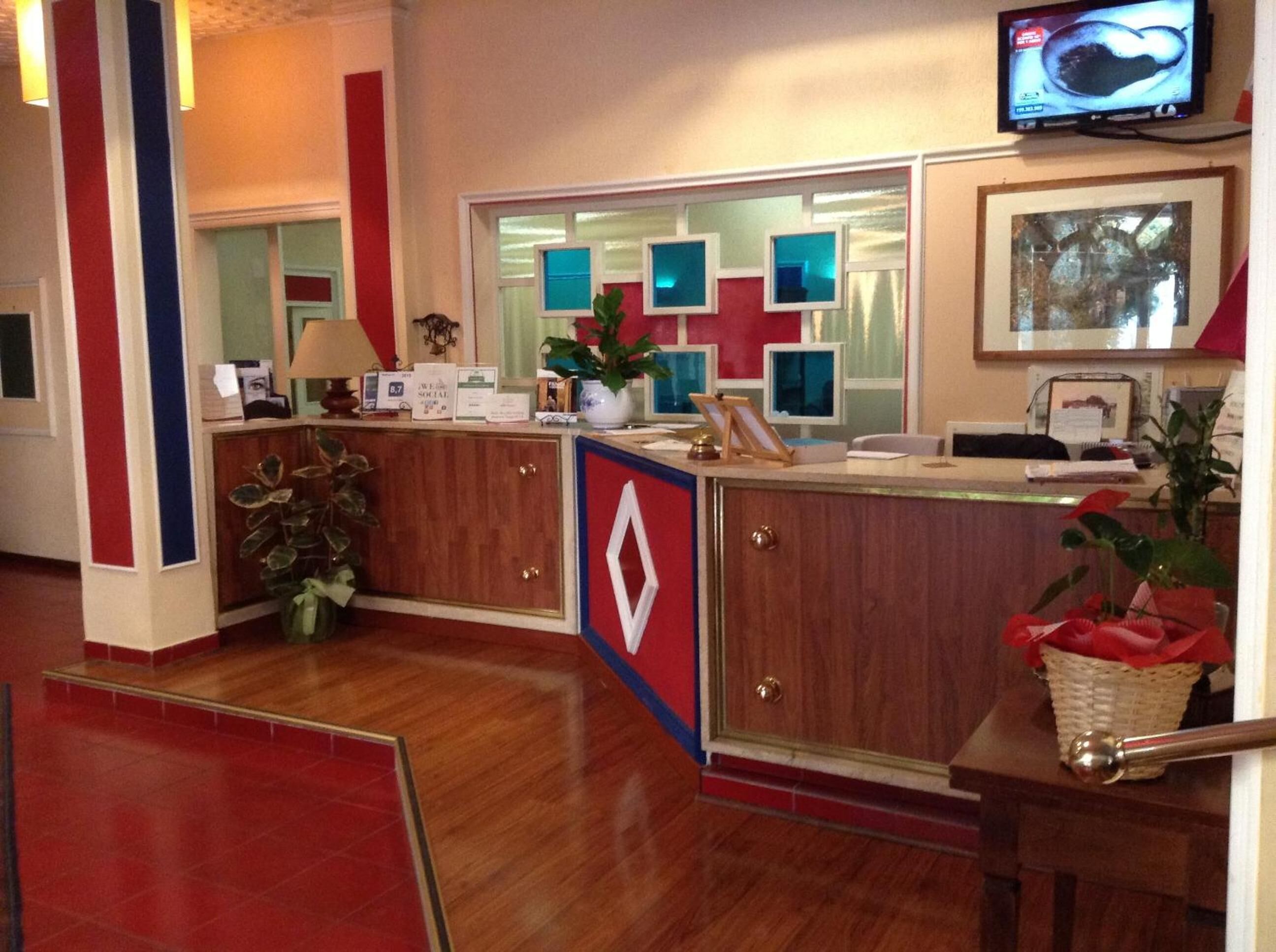 A reception area with a wooden desk, a television mounted on the wall, and a framed picture above the desk.