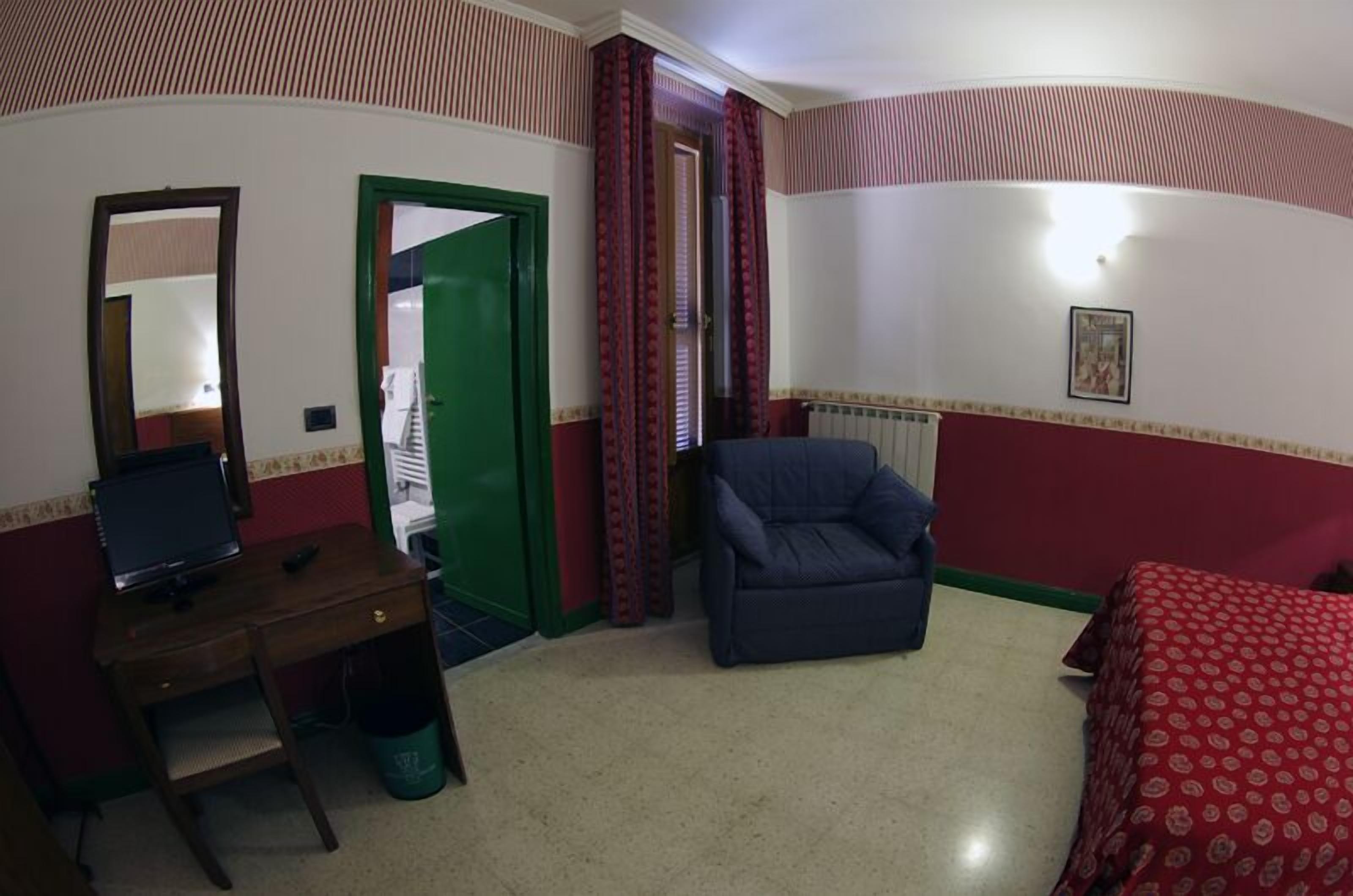 A hotel room with a bed, a desk with a computer, a chair, and a door leading to a bathroom.
