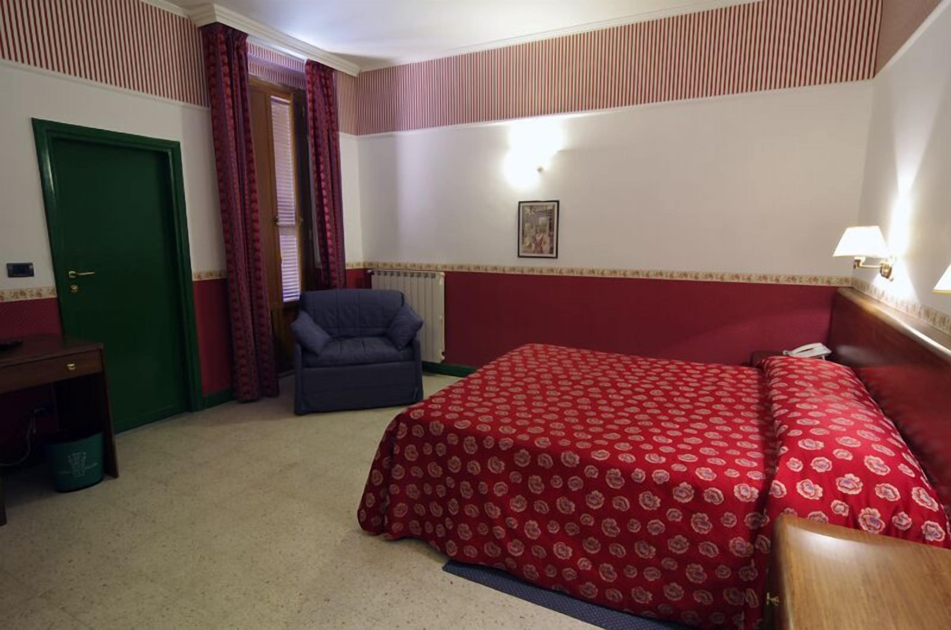 A hotel room with a bed, a chair, a desk, and a green door.
