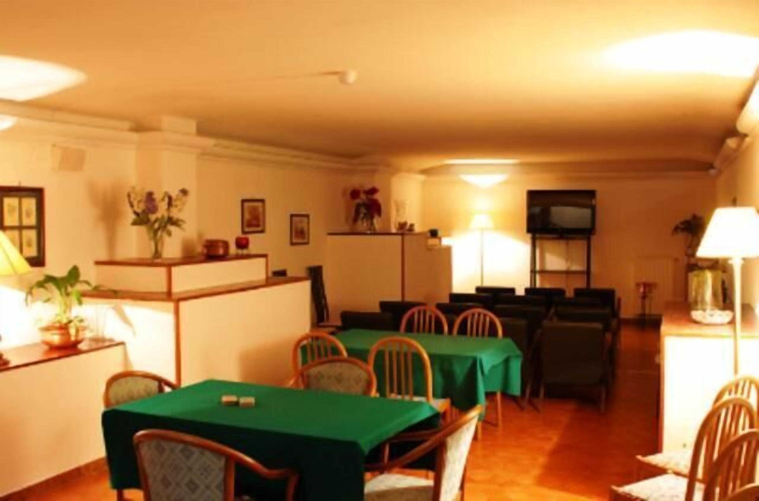 A dining area with tables covered in green tablecloths and wooden chairs.